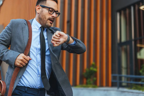 Resmi giyinmiş profesyonel bir adam acele eder ve saati kontrol eder, aciliyet ve iş faaliyetlerini vurgular.