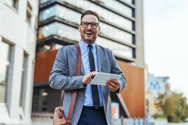 Tablet kullanırken takım elbiseli başarılı bir işadamı güvenle gülümsüyor. Çağdaş mimarinin yanında yakalanan, profesyonellik, pozitiflik ve kentsel kurumsal bir ortamda başarı..