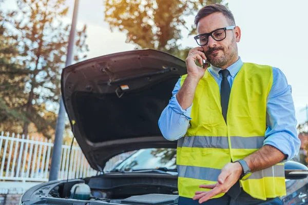 Yansıtıcı yelek giymiş bir adam güneşli bir günde bozuk bir arabanın yanında telefon görüşmesi yapıyor. Aracın bozulması ve yol yardımı için yardım istiyor gibi görünüyor..