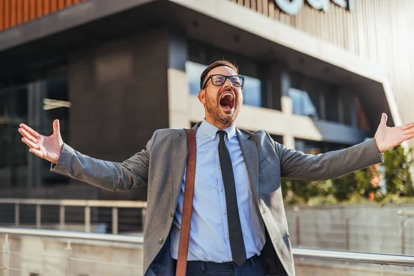 Neşeli bir işadamı modern bir ofis binasının önünde sevinçten havalara uçuyor. Profesyonel bir ortamda başarının ve başarının mükemmel bir temsili..