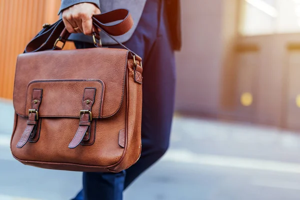 Bir işadamı şehir ortamında kahverengi deri bir çanta taşır. Görüntü profesyonellik, stil ve hareketlilik, iş ve seyahat temaları için idealdir.