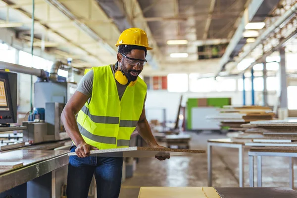 Koruyucu ekipman giyen fabrika işçisi endüstriyel bir ortamda ahşap maddeleri taşıyan makineler kullanıyor. Ahşap işçiliğine adanmış bir imalat ortamında güvenlik, teknoloji ve verimlilik göstergesi.