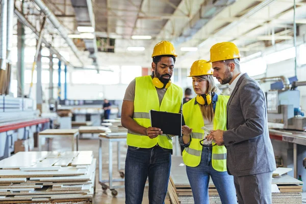 Endüstriyel bir ortamda çalışan çeşitli profesyonellerden oluşan bir grup, güvenlik teçhizatı ve aletlerle donatılmışken süreç ayrıntılarını tartışıyor. Modern bir üretim ortamında işbirliği ve takım çalışması.