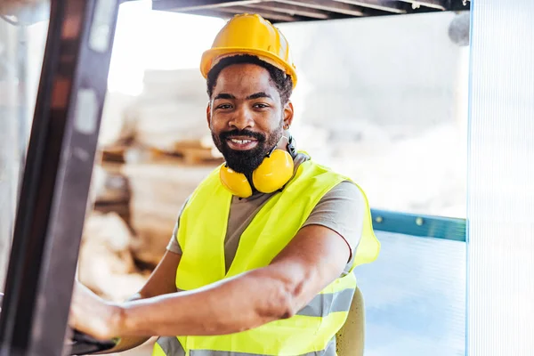Güvenilir bir inşaat işçisi güvenlik donanımı giyiyor ve depo ortamında gülümseyen bir forklift kullanıyor. İnşaat ve sanayi alanlarında profesyonellik, güvenlik ve adanmışlık temaları vurgulanıyor.