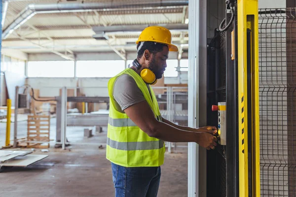 Sert şapka ve yansıtıcı yelek giyen bir sanayi işçisi, güvenlik ve verimliliği vurgulayarak fabrika ortamında makineler çalıştırıyor. Sahne profesyonellik ve endüstriyel otomasyon taşıyor.