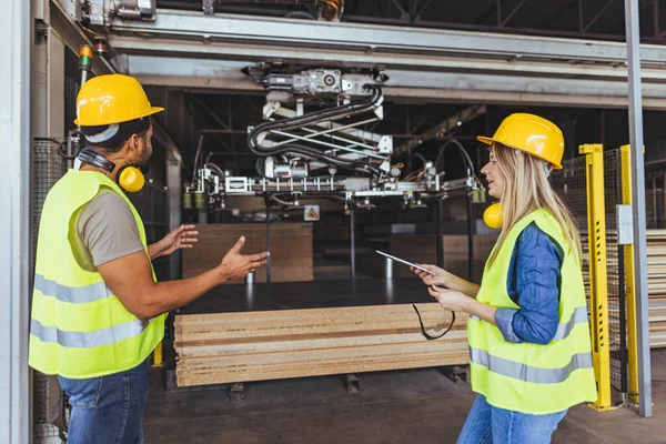 Güvenlik donanımlı işçiler fabrika katında gelişmiş makineleri çalıştırırken görevler hakkında konuşuyorlar.