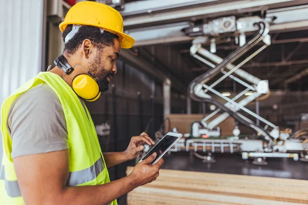 Koruyucu ekipman kullanan kendine güvenen işçiler, dijital tablet kullanarak modern endüstriyel makineleri çalıştırıyor, üretimi arttırıyor ve imalat tesislerinde iş güvenliğini sağlıyor..