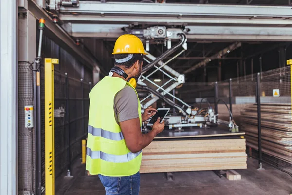 Bir endüstriyel fabrikada otomatikleştirilmiş makine ve materyalleri denetlemek için tablet kullanan güvenlik donanımlı bir erkek işçi, profesyonel bir imalat ortamında pürüzsüz işlemler ve üretkenliği sağlıyordu..
