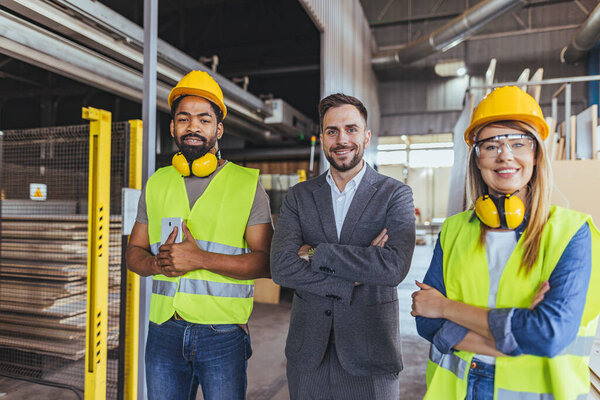 Diverse team of factory employees and a manager inside a production facility, representing teamwork, leadership, and industrial safety, wearing protective equipment like helmets and high-visibility vests.