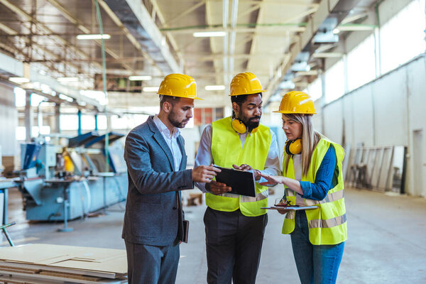Diverse team of factory employees and a manager inside a production facility, representing teamwork, leadership, and industrial safety, wearing protective equipment like helmets and high-visibility vests.