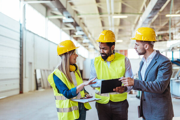 Diverse team of factory employees and a manager inside a production facility, representing teamwork, leadership, and industrial safety, wearing protective equipment like helmets and high-visibility vests.