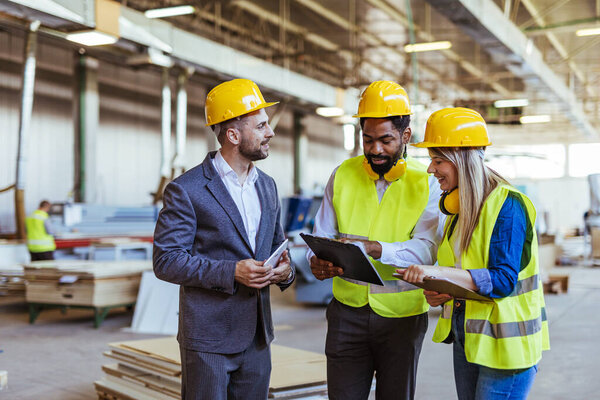 Diverse team of factory employees and a manager inside a production facility, representing teamwork, leadership, and industrial safety, wearing protective equipment like helmets and high-visibility vests.