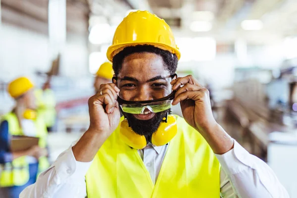 Endüstriyel fabrikada miğferi olan Afrikalı Amerikan işçisinin portresi.