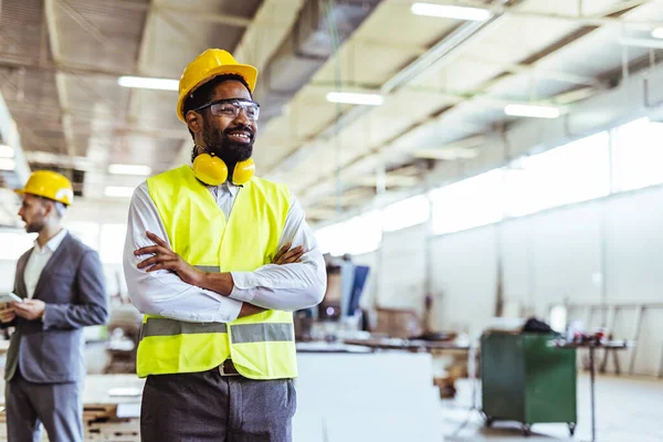 Gülümseyen Afro-Amerikan erkek işçi, profesyonel giyimli ve güvenlik teçhizatlı.