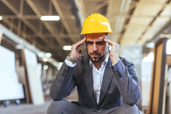 Sarı miğferi ve baş ağrısı olan genç bir mühendisin portresi.