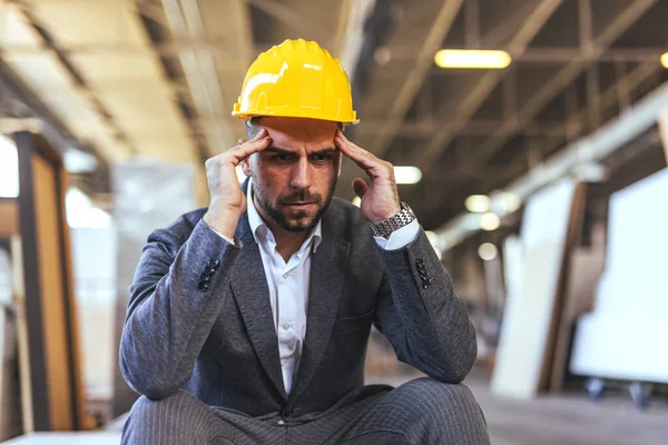 Sarı miğferi ve baş ağrısı olan genç bir mühendisin portresi.