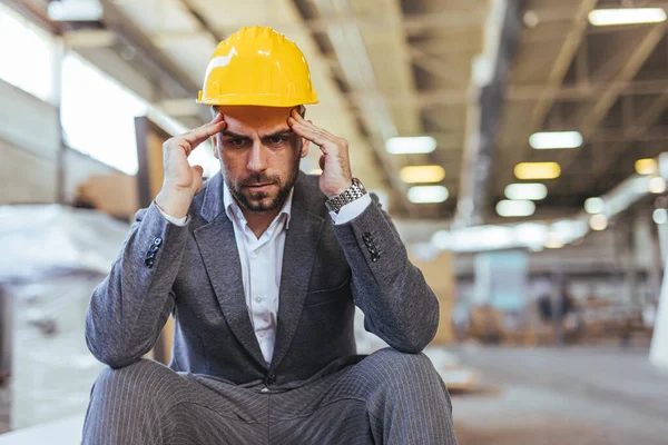 Sarı miğferi ve baş ağrısı olan genç bir mühendisin portresi.