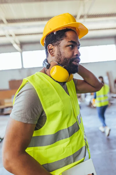 Depoda sarı kasklı ve boyun ağrısı çeken Afro-Amerikan erkek mühendis.