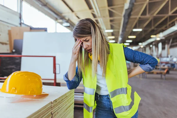 Endüstriyel bir çalışma alanında koruyucu giysi giyerken kafasını hayal kırıklığına uğratan bir kadın. Stres, işyeri güvenliği ve işçilerin fiziksel olarak çaba gerektiren ortamlarda karşılaştıkları zorlukları gösteriyor.