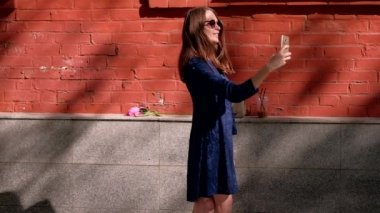 Slowmotion. Selfie fotoğraf kırmızı duvar, mavi elbiseli bir genç bir kadın yapar