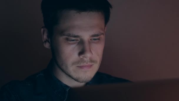 Retrato de un hombre trabajando en la computadora por la noche. Hombre navegando por Internet en habitación oscura . — Vídeo de stock
