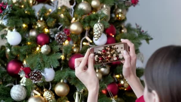 Hermosa mujer fotografiando en el árbol de navidad del teléfono inteligente en casa . — Vídeos de Stock