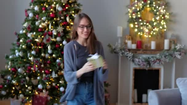 Hermosa mujer disfrutar de regalo de Navidad y salto de alegría, en el fondo del árbol de Navidad en casa decorada. Feliz Año Nuevo concepto . — Vídeos de Stock