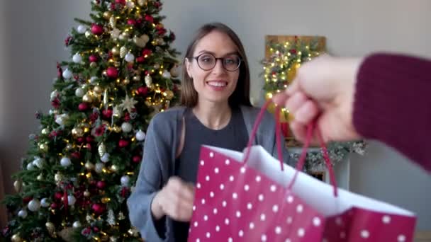 Gelukkige vrouw in glazen, ontvangt kerstcadeau op achtergrond van kerstboom in ingericht huis. Gelukkig Nieuwjaar concept. — Stockvideo