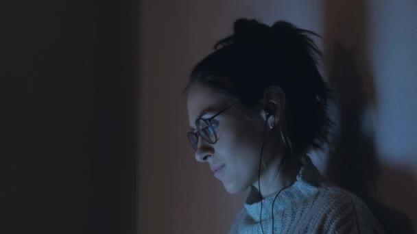 Las mujeres que trabajan en la computadora por la noche escuchan música con auriculares y bailan — Vídeos de Stock