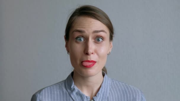 A Beautiful Girl Fools Around And Shows Her Tongue on Background of White Wall. — Stock Video