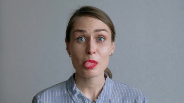 Een mooi meisje dwazen rond en toont haar tong op de achtergrond van witte muur. — Stockvideo