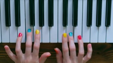 Güzel elleri ve renk manikür ile genç bir pozitif kız piyano oynuyor.