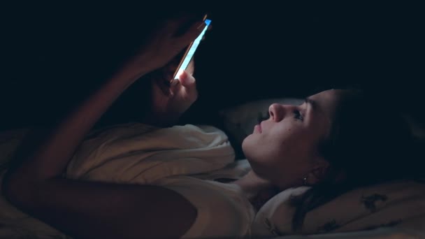 Жінка використовує мобільний телефон і лежить на ліжку вночі — стокове відео