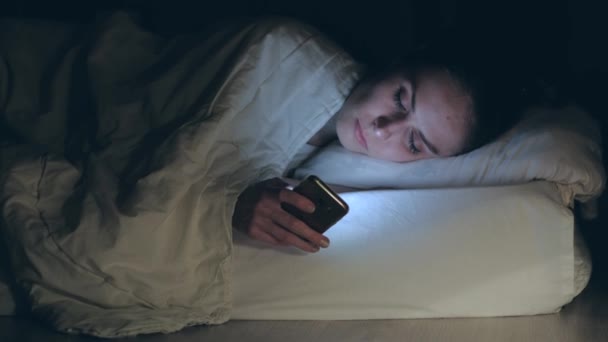 Mulher deitada na cama, adormece colocando e desligando smartphone . — Vídeo de Stock