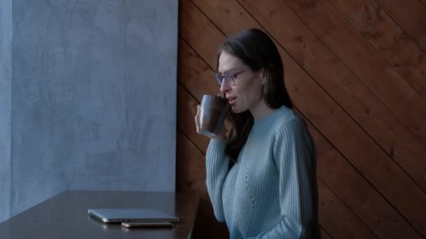 Söt tjej med laptop i caféet tittar i fönstret, dricker kaffe njuta av smaken. — Stockvideo
