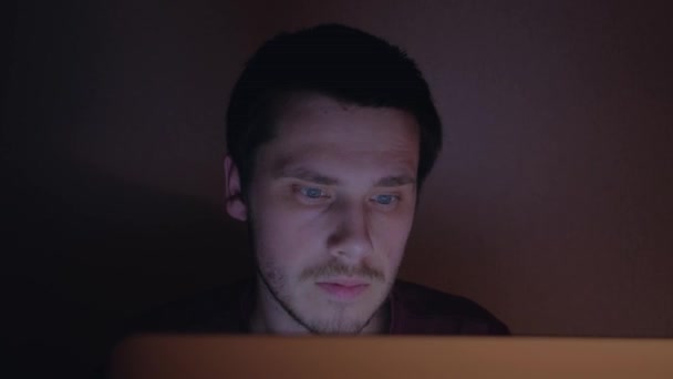 Porträt eines überraschten und schockierten jungen Mannes, der nachts mit Laptop arbeitet. — Stockvideo