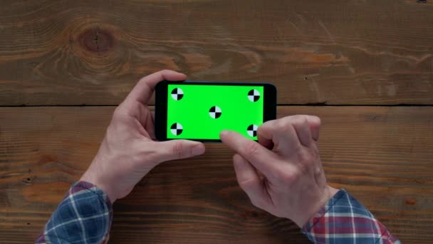 Άνθρωπος χρησιμοποιώντας smartphone με πράσινη οθόνη σε ξύλινο τραπέζι. — Αρχείο Βίντεο