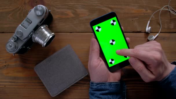 Fotograaf met smartphone met groen scherm op houten tafel. — Stockvideo