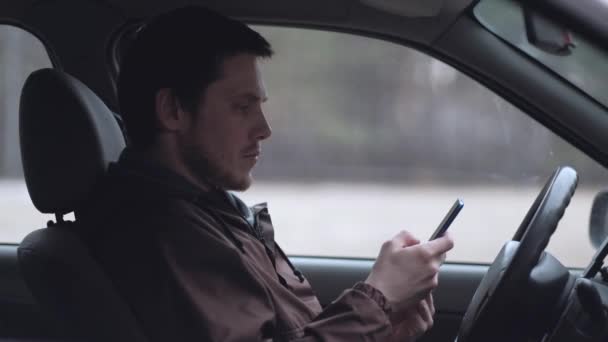 Ένας νεαρός άνθρωπος χρησιμοποιεί smartphone, κάθεται στην καμπίνα του αυτοκινήτου. — Αρχείο Βίντεο