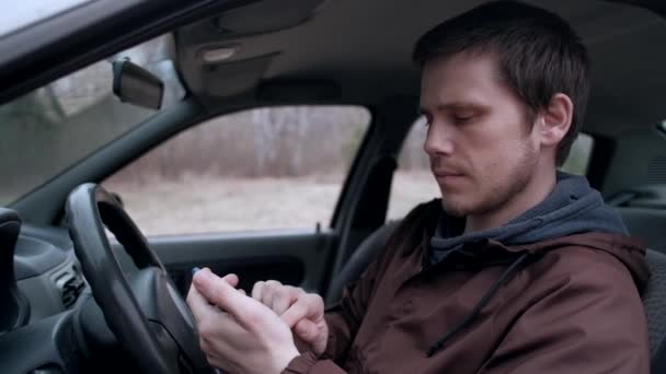 Un jeune homme utilise un smartphone, assis dans la cabine de la voiture . — Video