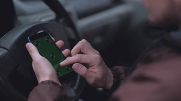 車の中で緑色の画面を持つスマートフォンを使用して男性ドライバー. — ストック動画