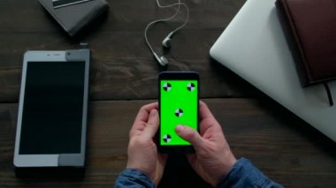 Ahşap masadaki yeşil ekranlı akıllı telefonu kullanan adamın elleri..
