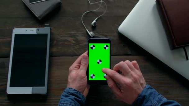 Mani dell'uomo utilizzando smartphone con schermo verde su tavolo in legno. — Video Stock