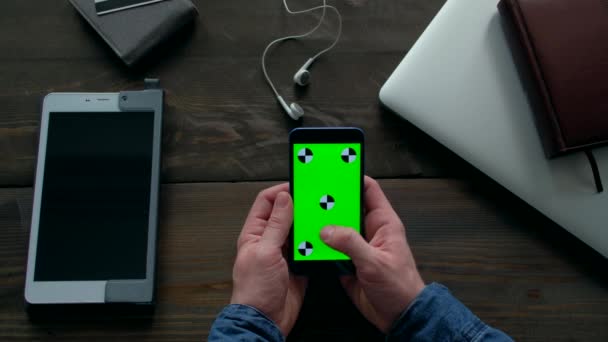 Menschenhände mit Smartphone mit grünem Bildschirm auf Holztisch. — Stockvideo