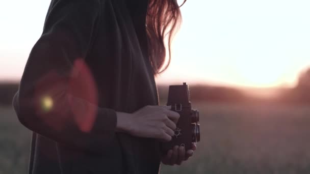 Femmina sta in campo con fotocamera vintage, sullo sfondo il tramonto con bagliore del sole — Video Stock