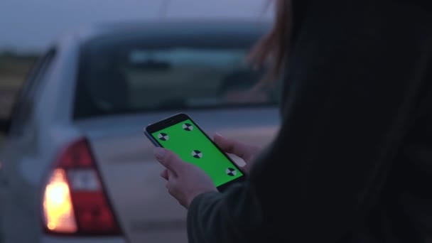 Vrouw met een smartphone met groen scherm op de achtergrond van gebroken auto. — Stockvideo