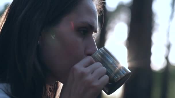 Kvinna dricksvatten från järn Mugg i skogen på bakgrunden av solen bländning. — Stockvideo