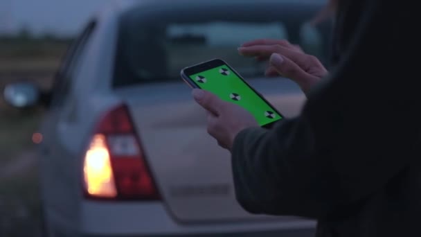 Mujer sosteniendo un teléfono inteligente con pantalla verde en el fondo del coche roto . — Vídeo de stock