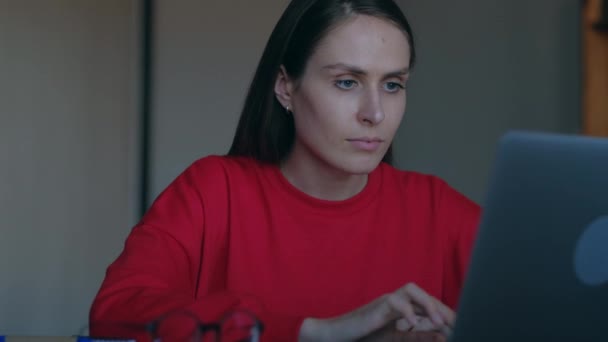 Vacker ung kvinna med röd tröja arbete på laptop i hemmet. — Stockvideo