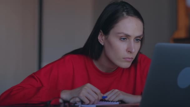 Schattige vrouw overschrijft in Kladblok informatie van de laptop. — Stockvideo